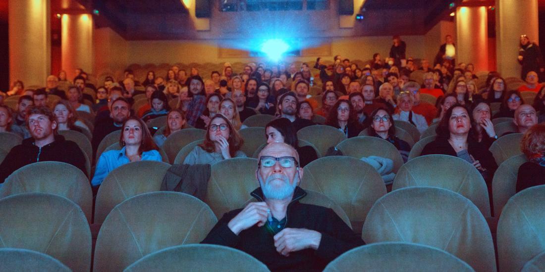 People sitting in a cinema, facing the screen with a projector beaming behind them