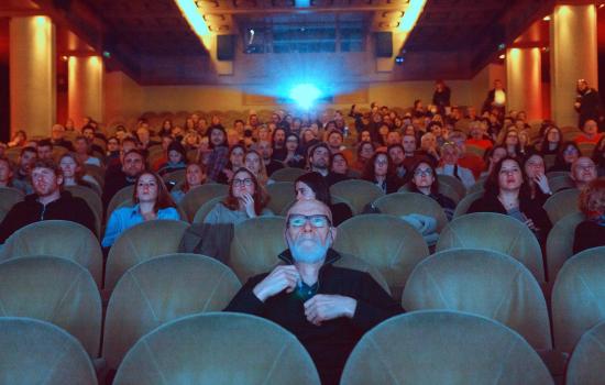 People sitting in a cinema, facing the screen with a projector beaming behind them