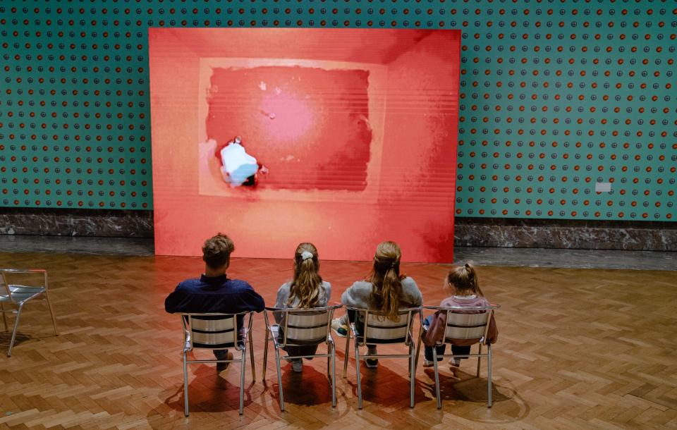 The image shows a family with children admiring a work by John Baldessari at Bozar