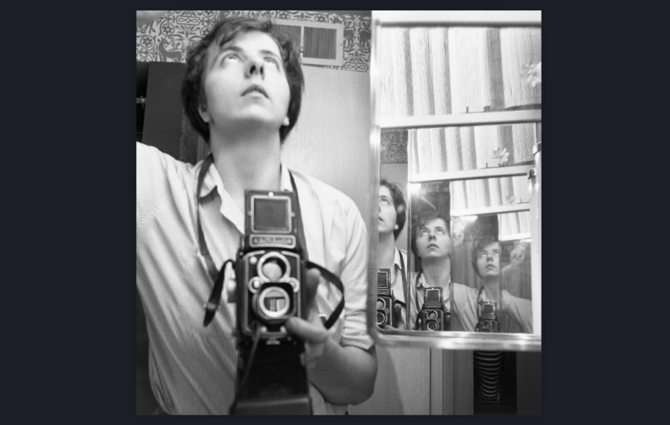 Zwart-witfoto van vrouw die omhoog kijkt en haar camera op een spiegel richt die haar verschillende keren weerspiegelt